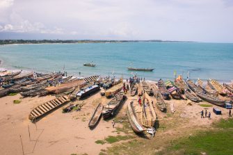 A landscape shot of a coast line. On the beach in the foreground are small canoe-like boats.