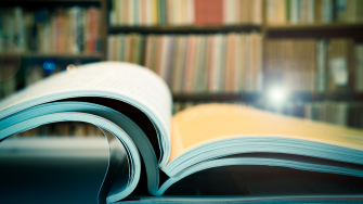 Piles of books and magazines on background of book shelf, with lens flare