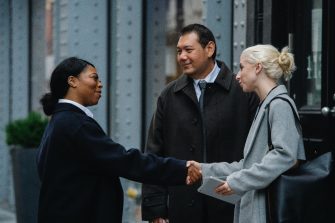 Two women shaking hands standing next to a man
