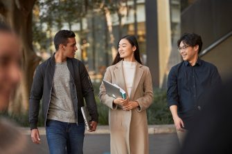 Three law students walking in front of Law Building, walking towards the camera, greenary and reflections in glass of Law Building in background