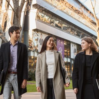 Three Law students walking on Main Wallkway with the Law Building in the background, dressed in smart attire and winter coats