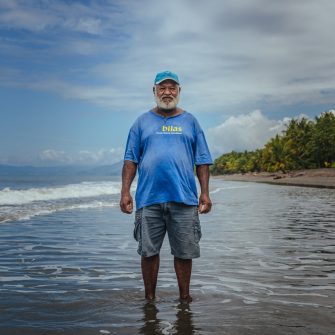 One of the community leaders in Kahingi stands where his gardens used to be over a decade ago before being slowly swept away into the sea. For years this community would see their beach-side homes slowly erode into the ocean without understanding what was happening until IOM staff