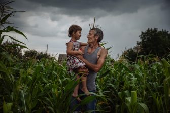 Valerii Grek	“The more i get to know people, the more I like dogs. Sometime we even limit expenses on our own food in order to feed our dogs. They feel me. When I leave, they wait for me at the gates. They are my real friends. They are my family.”	“The more I get to know people, the more I like dogs,” says Valerii, quoting Mark Twain as he sits with his family and his dogs at a rickety table at the farm in the Eastern Ukrainian village ofNovyi Donbas. He’s lived here for the last four years, since the long and deadly conflict in the area forced him to abandon his happy life. Seven years he had been working on his perfect house in Dokuchaevsk, and welcomed the first granddaughter home. Then the conflict started. Shells rained down each evening at 5pm, and when his neighbour’s house took a direct hit he knew it was time to grab his family and go. 
 
Valerii, his wife, daughter, granddaughter and two dogs found an abandoned house: “just a shed really. Like he has done all his life, Valerii put his shoulder to the wheel and bit by bit he created a home. “The house had been empty for three years, but it was the only option for us. I saved money, and got the essential services in as as I want my girls to live in comfort,” he says. 
 
His income comes from some allowances from the Government of Ukraine, his market garden, and the hundreds of chickens which populate the outhouses. “I have regular customers at the market, and I can sell my stock in half an hour at the local market. My customers are urging me to bring more,” Valerii smiles. 
 
As a displaced person, he was eligible to apply for small grants, and IOM provided him with a rotary cultivator for his burgeoning garden. 
 
“I was left with nothing, I started from scratch, and I will achieve something, as long as I have strength,” says Valerii. 
 
Two of his dogs, Lyalya and Dusya follow him around the yard, apparently listening to his every word. “They feel my emotions. When I leave, they wait for me at the gates. They are my real friends. They are part of my family.”
 
The canine family is thriving. Lyalya’s son, Khitriwas born in Novyi Donbas. And a fourth dog, Richard, turned up one day. “He was homeless, like we were once. So how could we walk on by?”