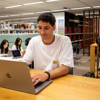 A student inside a Main Library group study area, looking at his laptop.
