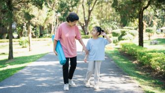 Happy grandmother and granddaughter walking together in a sunny park, carrying yoga mats, enjoying outdoor activities and quality time in nature