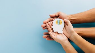 Adult and child hands hold a brain jigsaw in a head paper cut for Down Syndrome awareness. Highlighting global Down Syndrome Day and Autism Awareness with care and support.