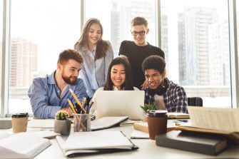 Multinational happy students gathering in library, using laptop and doing their project