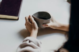 woman in white jumper holding cup talking