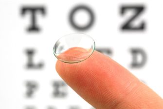 Contact lens on finger and snellen eye chart. The eye test chart is shown blurred in the background.