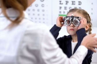 Pretty little schoolgirl visiting oculist for measuring eyesight with phoropter
