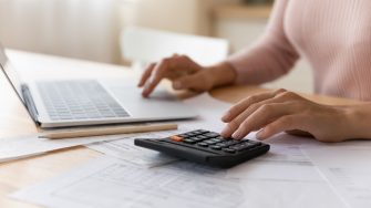 Close up cropped woman planning budget, using laptop and calculator, professional accountant calculating and paying domestic bills online, internet baking service, analyzing financial documents