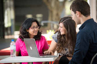 Two women and a man casually work at a laptop