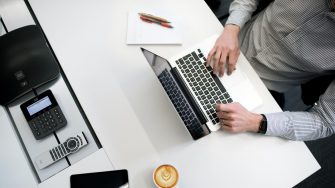 Aerial image of man using laptop on white desk with capuccino