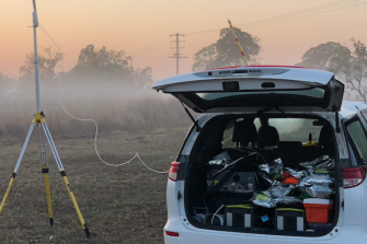Car parked in misty field wiht boot open and large antenna set up nearby