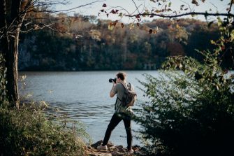 Man with backpack taking picture beside lake