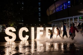 Kids in front of SciFest outdoor sign at nighttime