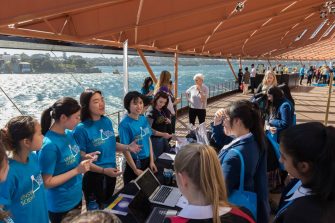 Group of students wearing blue tshirts near the water, with a table with laptops