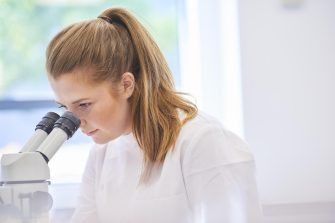 A female research scientist is analysing a sample on her microscope in a lab