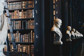 Line of statues extending into the distance in froft of staggered book shelves, in reverse