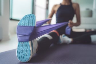 Woman using resistance band, doing yoga indoors on a mat.