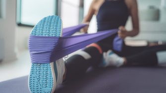 Woman using resistance band, doing yoga indoors on a mat.