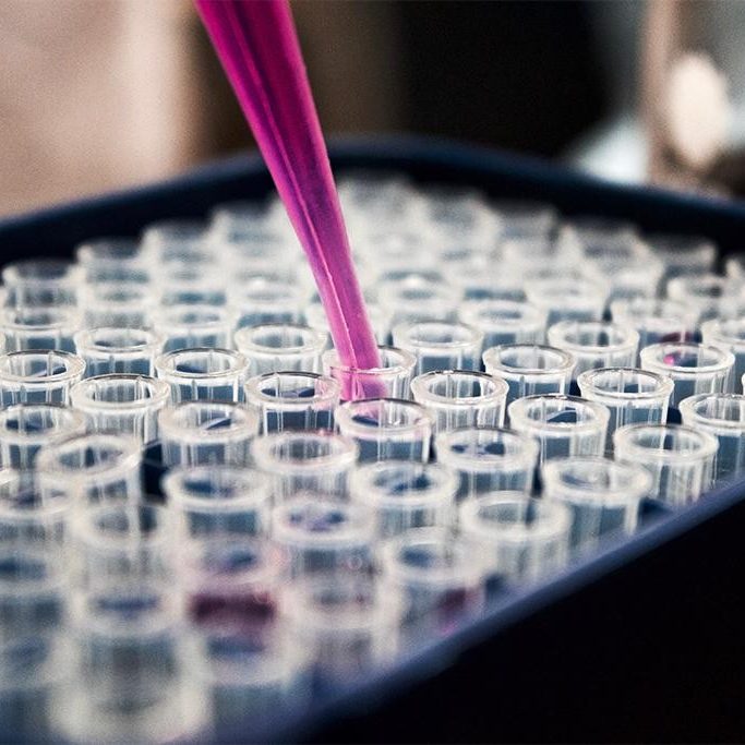 Rows of test tubes, one being filled by a purple syringe