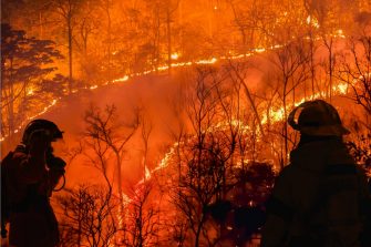 Muddy flood water surrounds a group of houses, with water almost up to the roof and roads completely covered
