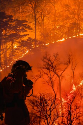 Muddy flood water surrounds a group of houses, with water almost up to the roof and roads completely covered