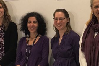 Row of people standing against a wall, gentleman on the far left holding Stand Up Stand Out poster