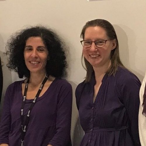 Row of people standing against a wall, gentleman on the far left holding Stand Up Stand Out poster