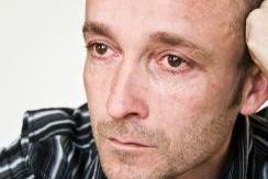 A man stares off into the distance with red ringed eyes