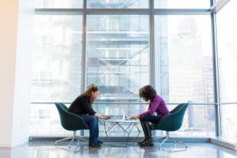 2 women on laptops in a big glass building 