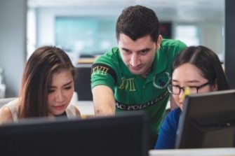 Man helps 2 females on a computer