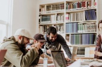 3 men gathered around a laptop laughing 