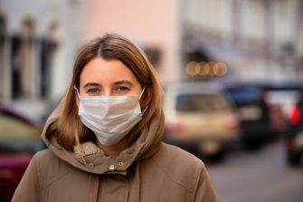 A young woman in a parker wears a surgical mask
