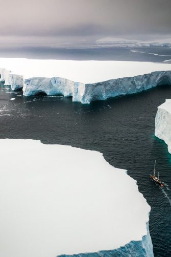 Aerial view of a large iceberg floating near an ice shelf under grey skies 0