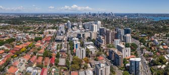 Looking down over units, high rises buildings towards Sydney city with the harbour and a blue sky on the horizon.