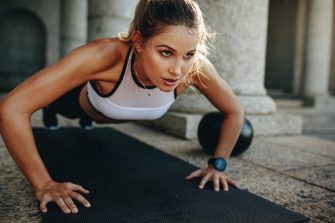 Close up of a woman doing fitness training with a medicine ball by her side. Fitness woman doing push ups on a training mat.