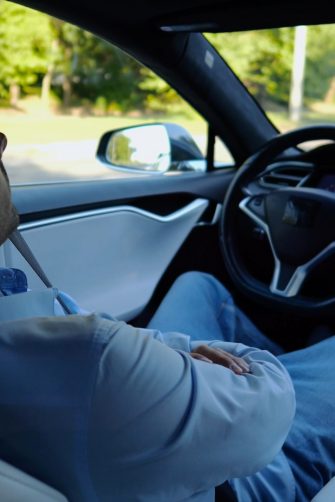 Male businessperson experience to ride an autonomous self driving electric car at urban road. Confident businessman resting during riding on electrical auto with autopilot at city. Slow mo