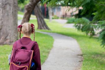 A girl wearing maroon and white school uniform walking to school alone. School students return to classrooms after COVID-19 outbreak in Australia
