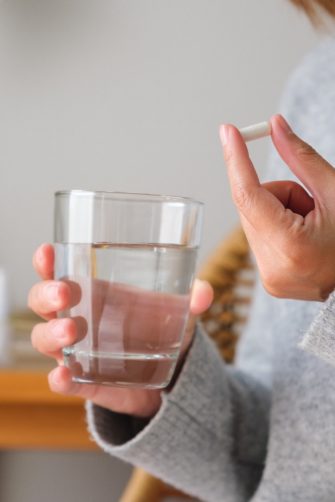 Closeup image of a woman holding white pills and a glass of water