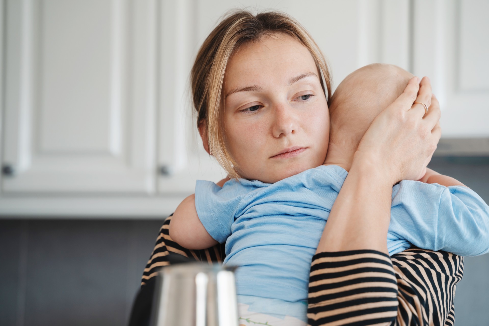 Tired sleepy mother taking care of sick baby at home. Young exhausted woman with toddler at home. Loving mother hugging and comforting crying little son.