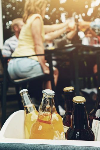 Group, people and drinks at barbecue in backyard, summer and vacation for holiday, celebration or event. Friends, cheerful and bbq with cooler box for dinner, party or reunion with alcohol in America.