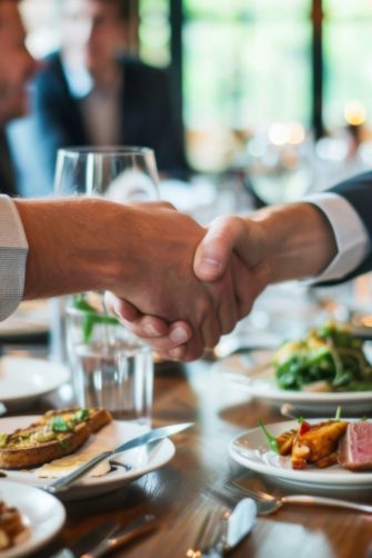 a group of people sitting at a table shaking hands business lunch sealing important deals