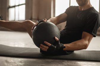 Side view of crop unrecognizable athletic male doing side twist exercise with medicine ball during intense functional training in gym