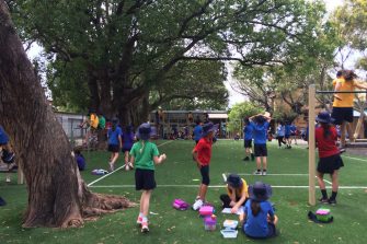 A group of primary school children do handstands on a grassy patch in a school playground