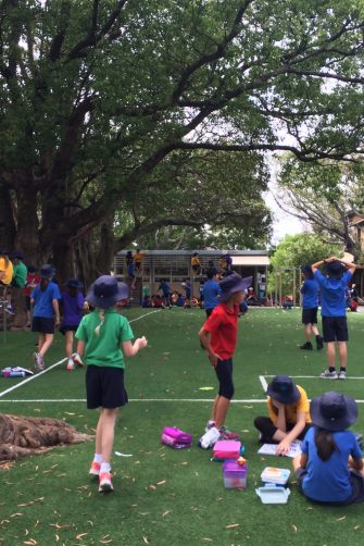 A group of primary school children do handstands on a grassy patch in a school playground