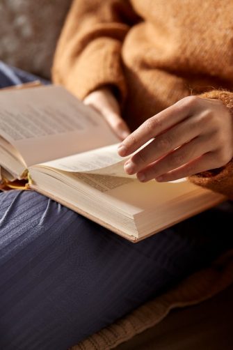 close up of woman in warm sweater reading book at home