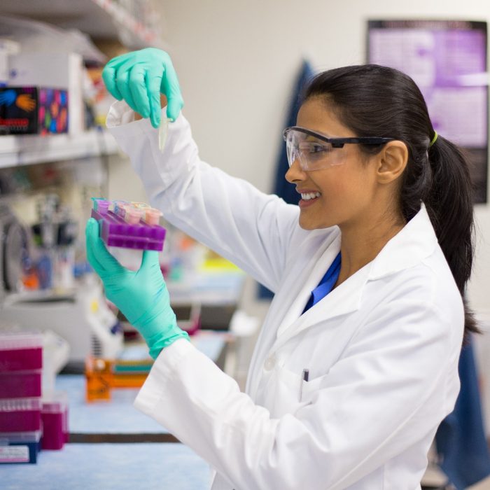 Closeup portrait, young scientist in labcoat wearing nitrile gloves, doing experiments in lab, academic sector.