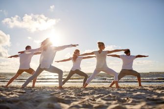 fitness, sport, yoga and healthy lifestyle concept - group of people making warrior pose on beach